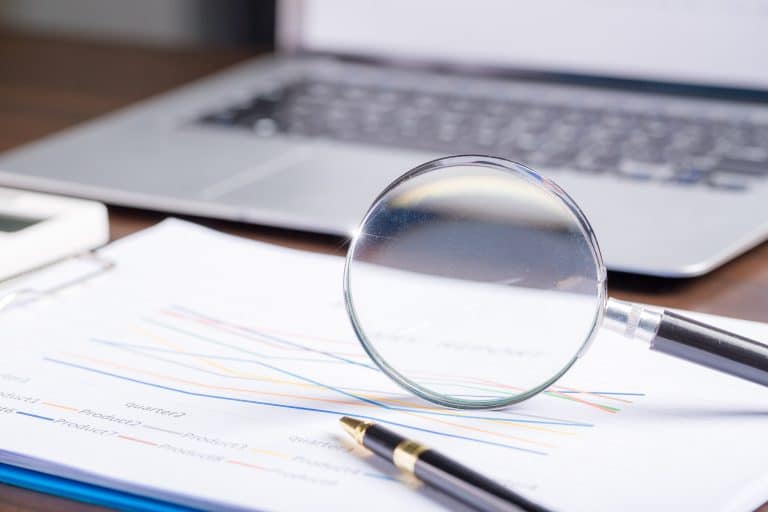 magnifying glass with business document financial paper chart statistic report on desk in office, closeup calculating machine with paperwork on table concept for analysis, market, banking